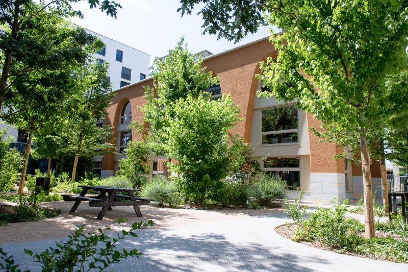 Un îlot de fraîcheur composé de mobilier en bois, de nombreux arbres et d'un jardin de pluie au jardin de l'Îlot B2 à Lyon Confluence