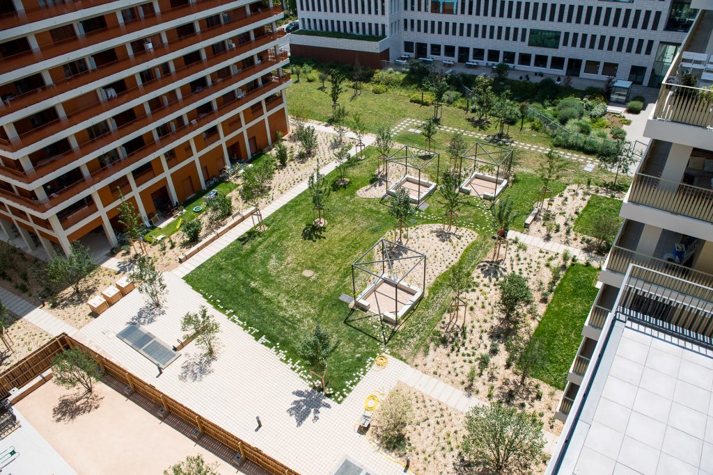 Des pavés, des composteurs, des structures aciers avec des plantes grimpantes, des massifs plantés, des arbres et du mobilier en bois à la résidence Natural Square à Lyon