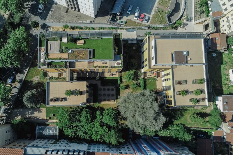 Vue aérienne du jardin de la résidence 25 place Croix-Rousse avec des plantations, des toits végétalisés, des bacs acier, des jardinières, un terrain de pétanque et des arbres