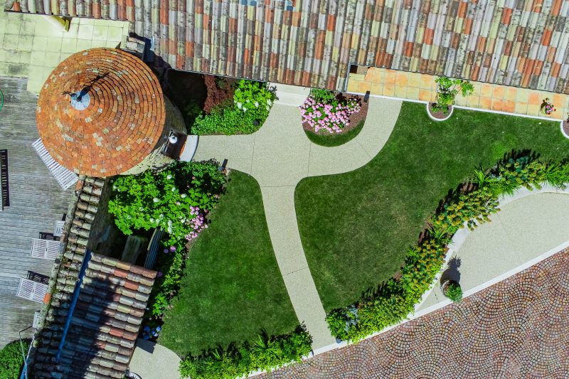 Vue aérienne d'un jardin de particulier avec gazon, massifs fleuris, cheminements en dalles et terrasse en petits pavés