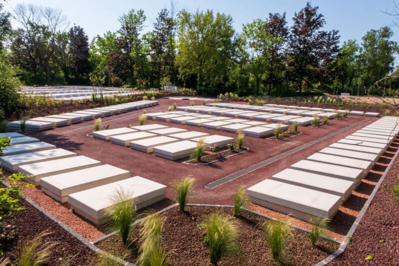 Un cimetière végétalisé avec des tombes blanches alignés et autour des massifs végétaux